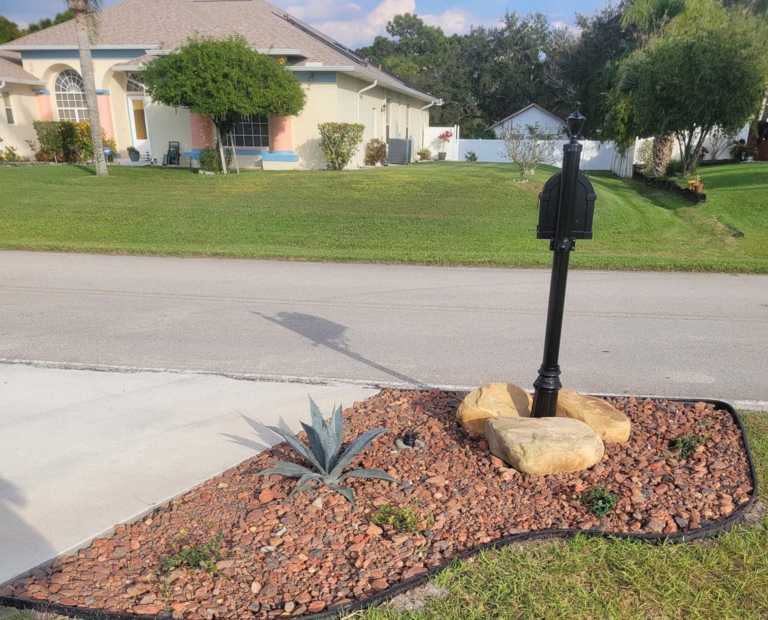 After: curved red-rock bed with boulders, an agave and black edging around the mailbox