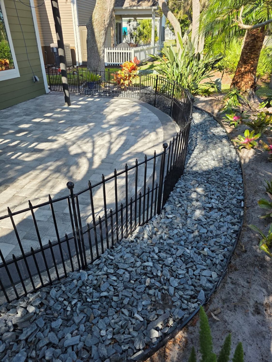 Paver patio with a black fence and a gray rock border with steel edging